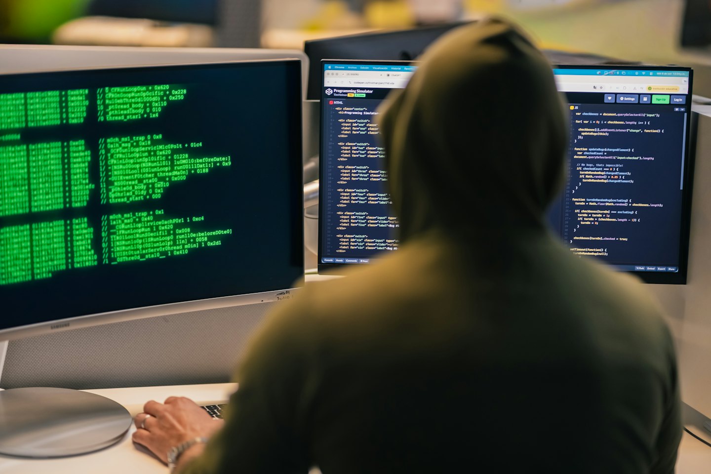 Programmatore con felpa lavora su due monitor con codice.
